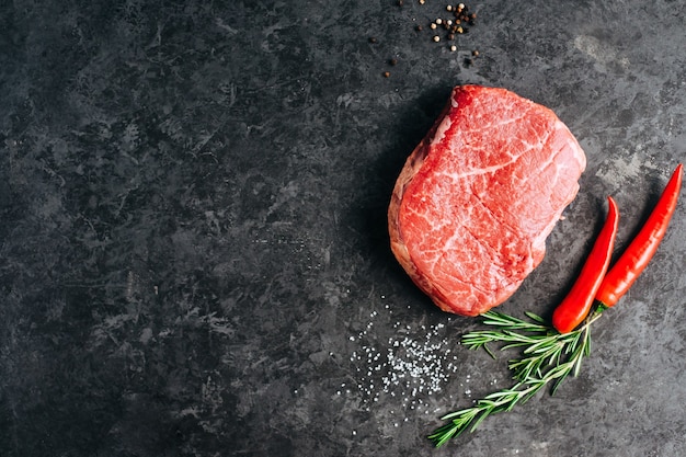 Steak de boeuf cru sur fond noir avec piment de romarin et épices copy space