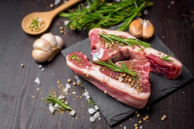 Steak de boeuf cru frais et ingrédients sur planche de pierre noire sur table en bois noir