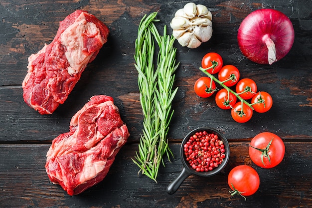 Steak de bœuf cru marbré biologique. Chuck eye roll avec oignon rouge romarin, grains de poivre à l'ail et tomates sur la vieille table en bois sombre