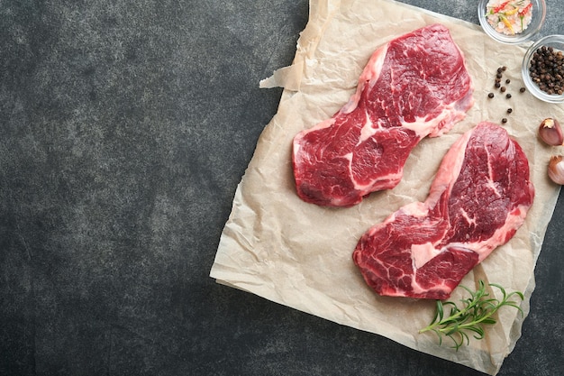 Steak de bœuf cru Marbré de côtes crues fraîches avec du sel et du poivre au romarin sur une planche à découper sur fond de béton foncé Steak de bœuf cru et épices pour la cuisson