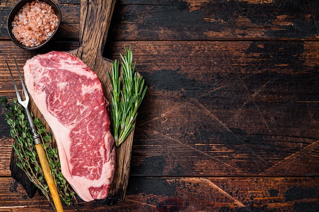 Steak de boeuf cru de New York ou contre-filet sur une planche de bois