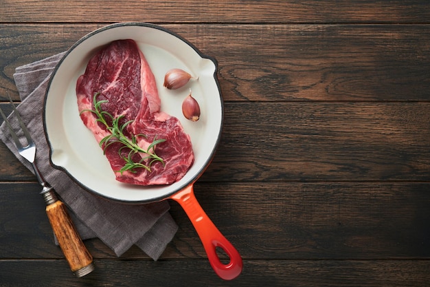 Steak de boeuf cru Steak de Ribeye frais cru avec sel et poivre de romarin dans une poêle en fer sur une planche à découper sur fond de béton foncé Steak de boeuf cru et épices pour la cuisson