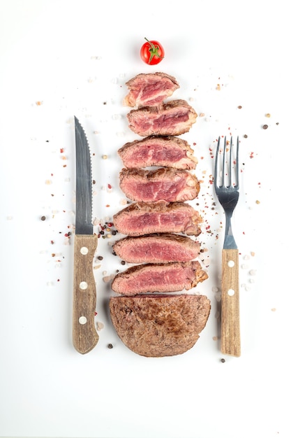 Photo steak de boeuf cuit frit coupé en morceaux avec des épices et des couverts sur fond blanc. vue de dessus.