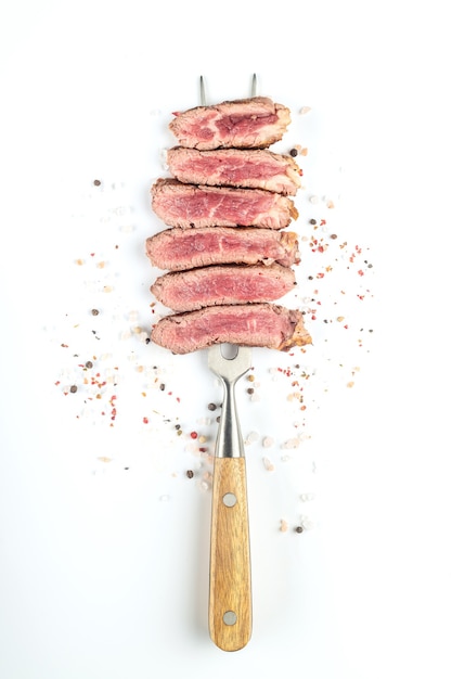 Steak de boeuf cuit frit coupé en morceaux avec des épices sur une grande fourchette à viande sur fond blanc. Vue de dessus.