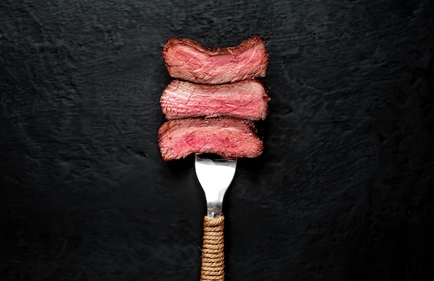 Steak de boeuf sur fourche sur béton foncé
