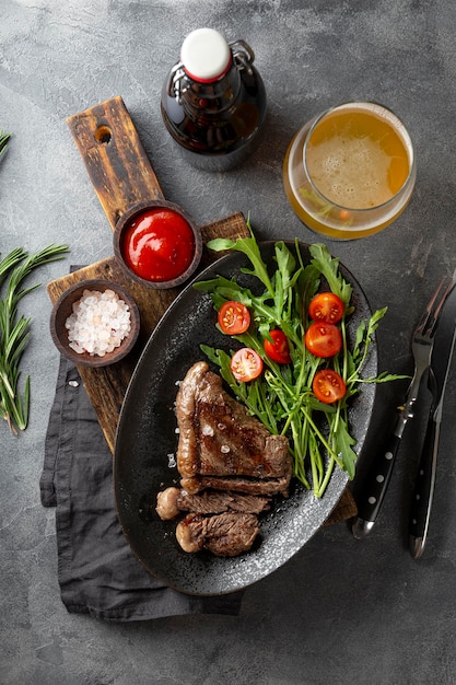 Steak de bœuf grillé bien fait avec une salade de légumes frais et un verre de bière légère