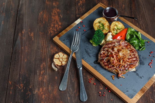 Steak de boeuf grillé cuit au barbecue, gros plan sur fond de table en bois foncé. Viande rouge rôtie juteuse fraîche sur une planche en pierre noire, poivre et romarin.
