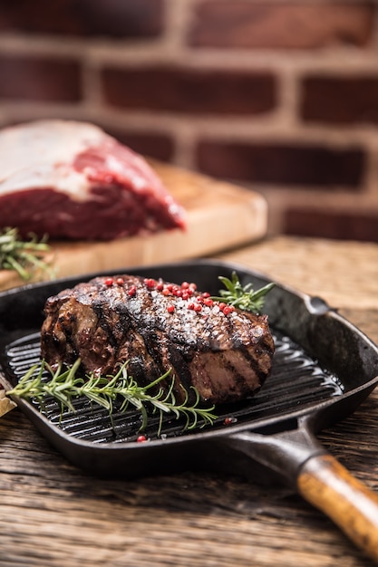Steak de boeuf grillé dans une poêle à griller avec du romarin aux herbes sur une table en bois.