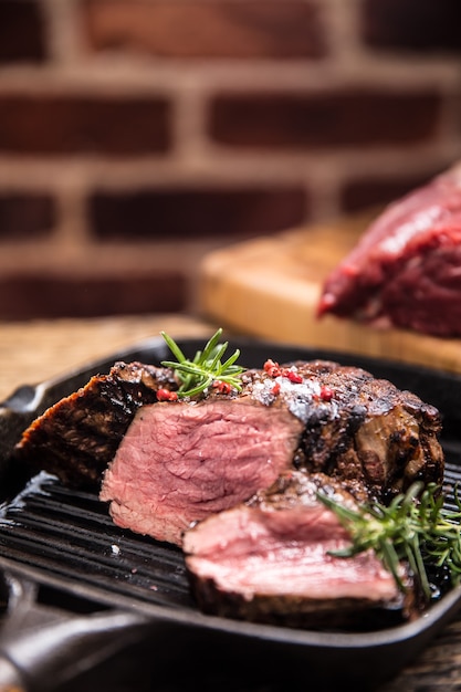 Steak de boeuf grillé dans une poêle à griller avec du romarin aux herbes sur une table en bois.