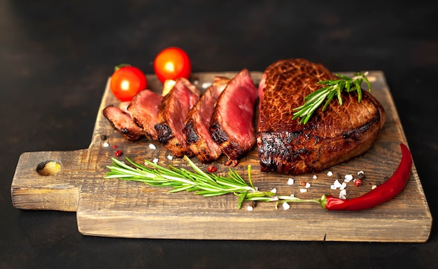 Steak de boeuf grillé, herbes et épices sur une planche à découper sur un fond de pierre, vue du dessus