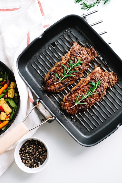 Steak de boeuf grillé avec légumes et romarin dans une poêle noire sur la table.