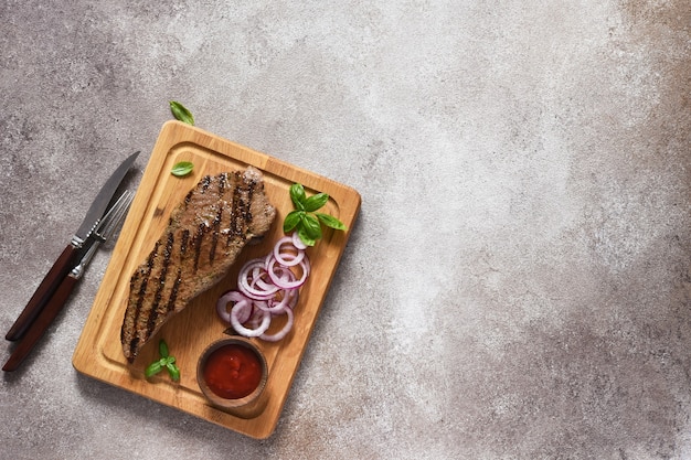 Steak de boeuf grillé avec sauce tomate et oignons rouges marinés sur une planche de bois. Vue d'en-haut.