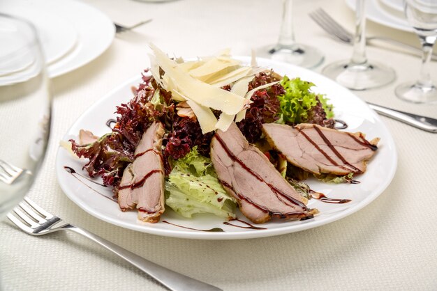 Steak de boeuf grillé tranché avec salade de feuilles vertes sur une assiette rustique avec des couverts.