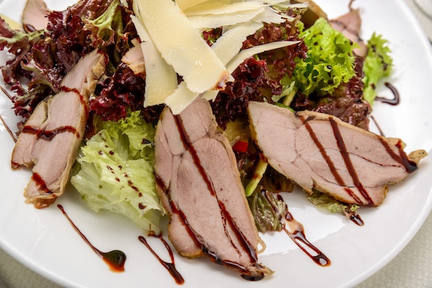 Steak de boeuf grillé tranché avec salade de feuilles vertes sur une assiette rustique avec des couverts.