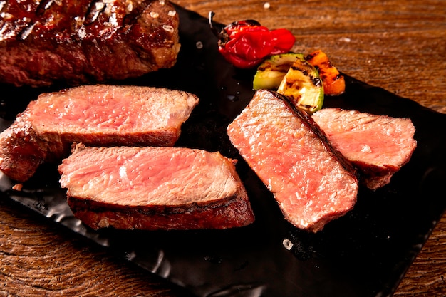 Steak de boeuf grillé en tranches sur une planche à découper noire sur la table en bois.