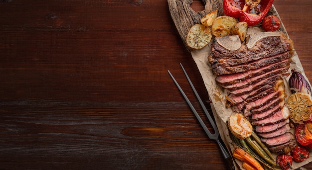 Steak de boeuf marbré sur l'os cuit à un état de grill moyen moyen. à côté du steak, des légumes grillés servant d'accompagnement. charmant dîner de gala pour deux