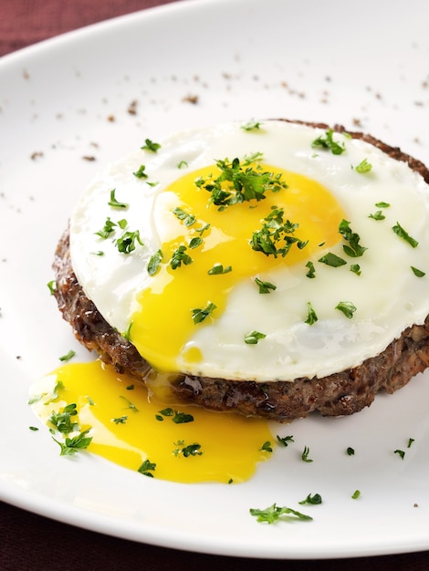 Steak de boeuf avec oeuf au plat sur plaque blanche.