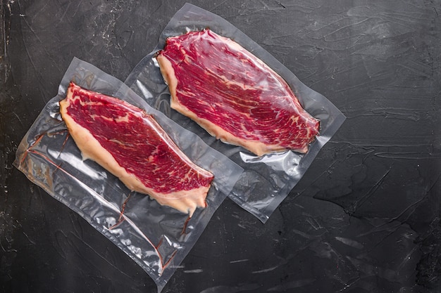 Steak de boeuf Picanha dans un sac scellé sous vide sur fond texturé noir, espace vue de dessus pour le texte.