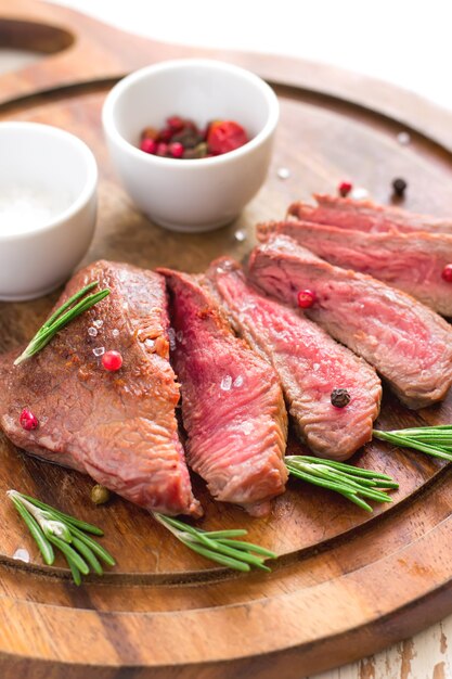 Steak de boeuf rôti coupé en tranches avec du romarin sur une planche à découper en bois