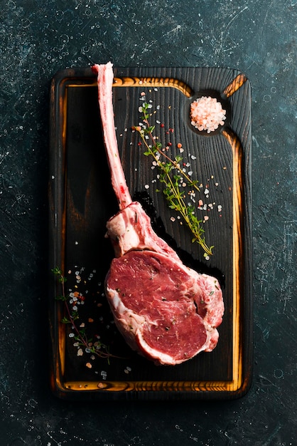 Steak de boeuf tomahawk cru vieilli à sec avec des ingrédients sur fond de pierre noire Vue de dessus Mise à plat