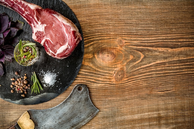 Steak de boeuf tomahawk cru vieilli à sec avec des ingrédients pour griller sur fond de bois. Vue de dessus. Espace de copie. Nature morte. Mise à plat