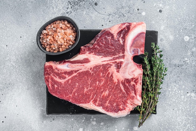 Steak de bœuf wagyu vieilli et sec brut Tbone non cuit sur planche de marbre avec thym Fond gris Vue de dessus