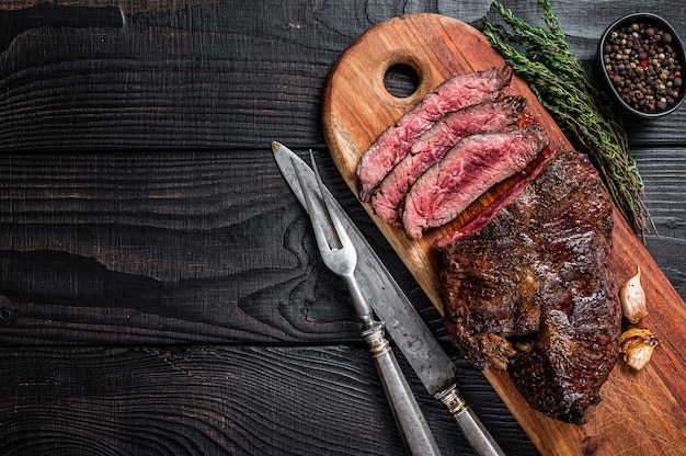 Steak de choix des bouchers grillés Onglet accrocher de la viande de boeuf tendre sur une planche à découper. Table en bois noir. Vue de dessus.