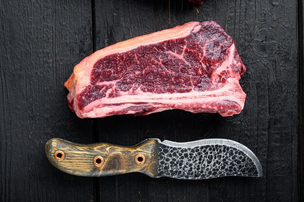Steak de club viande de boeuf marbrée crue sur fond de table en bois noir vue de dessus mise à plat