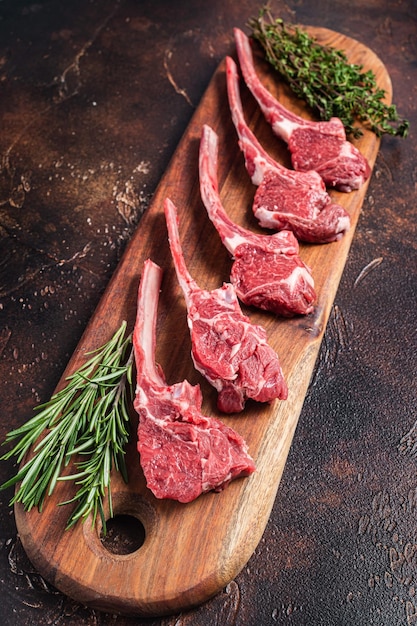 Steak de côtelette d'agneau cru sur planche de boucher avec romarin et thym Fond sombre Vue de dessus