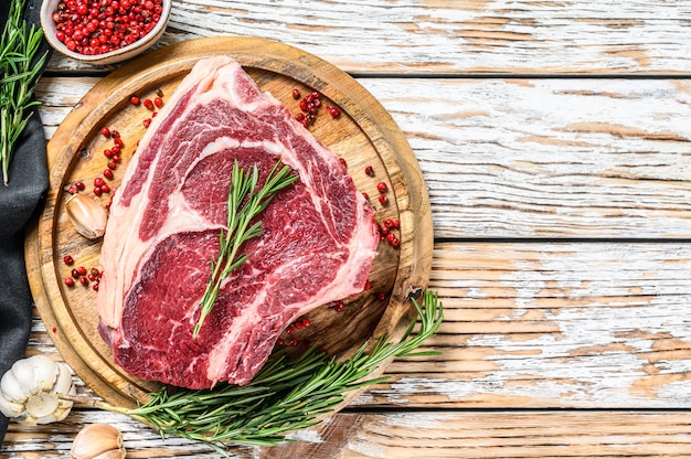 Steak de cowboy cru ou faux-filet sur l'os sur une planche à découper.