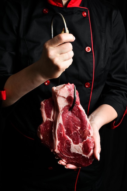 Un steak cru sur un crochet de viande dans les mains d'un chef Viande sur un fond noir