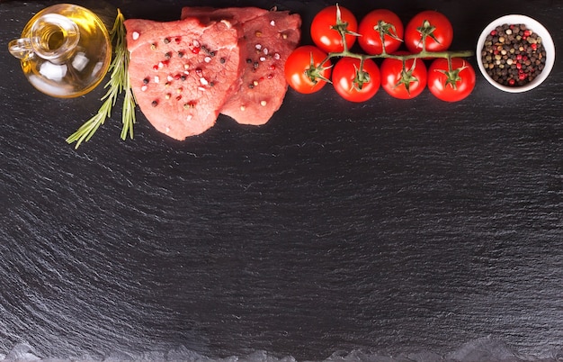 Photo steak cru avec des épices et des ingrédients pour la cuisson sur une surface en ardoise noire