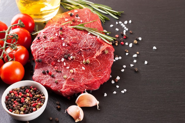 Steak cru avec des ingrédients de cuisine sur fond d'ardoise noire