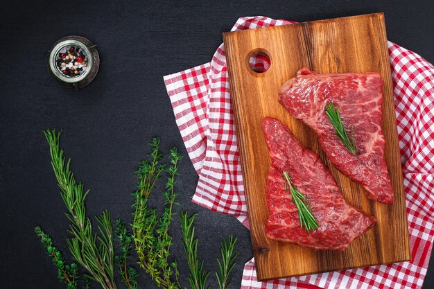 Steak cru sur une planche à découper avec du romarin et des épices