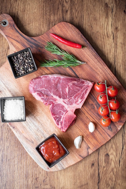 steak cru sur une planche à découper avec des herbes. Fond en bois.