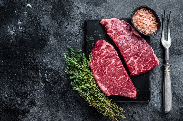 Steak de Denver cru frais Viande de boeuf en marbre aux herbes. Fond noir. Vue de dessus. Espace de copie.