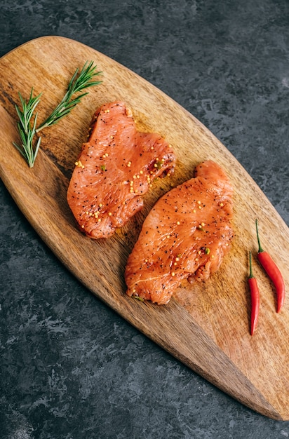 Steak de dinde mariné sur une planche de bois avec du romarin et du piment.