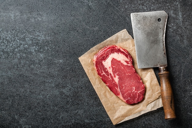 Steak de faux-filet cru et couteau de boucher sur tableau noir