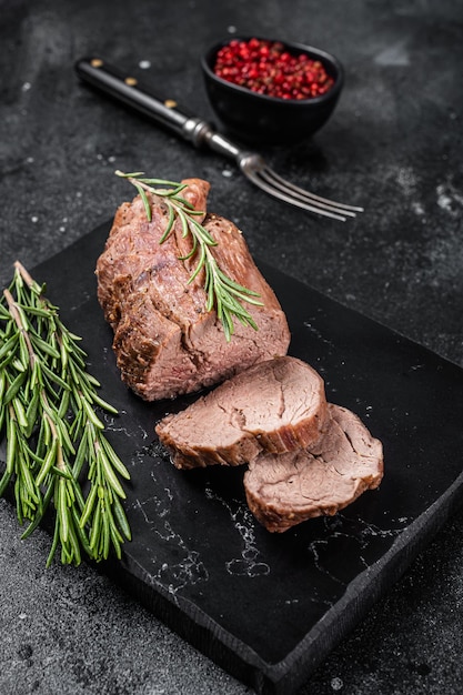 Steak de filet tranché, rosbif sur planche de marbre au romarin. Fond noir. Vue de dessus.