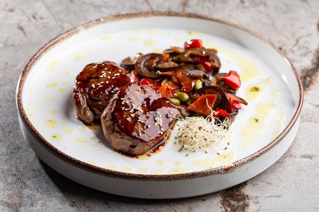 Steak de filet de viande grillé enveloppé dans des médaillons de bacon avec sauce aux framboises servi avec légumes et champignons