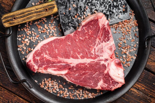 Steak florentin cru ou steak à os T viande de bœuf marbrée dans un plateau de cuisine en acier Fond en bois Vue supérieure