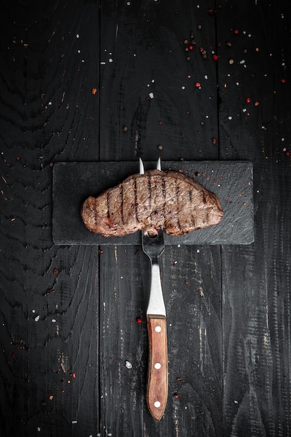 Steak sur fourche sur fond de bois foncé. bannière, lieu de recette de menu pour le texte, image verticale vue de dessus.