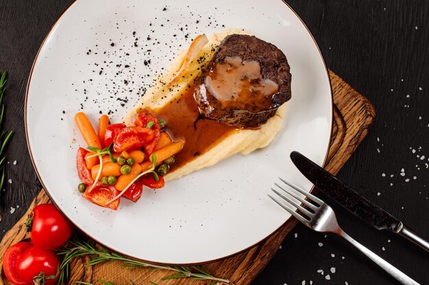 Steak frais savoureux avec purée de pommes de terre et légumes bouillis sur fond de bois