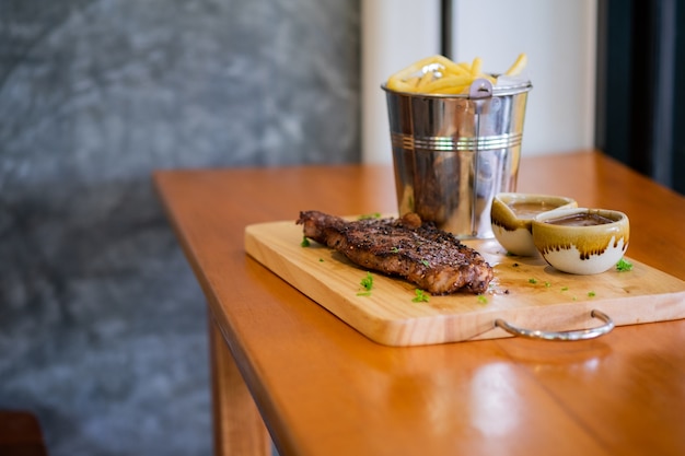 Steak avec frites et sauce sur un plateau en bois