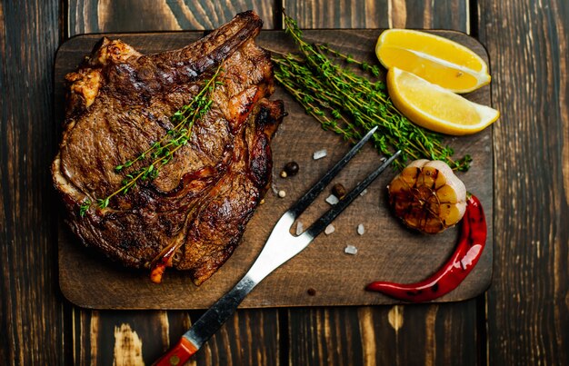 steak grillé sur une planche à découper avec citron, poivron rouge, ail et assaisonnement sur rustique foncé