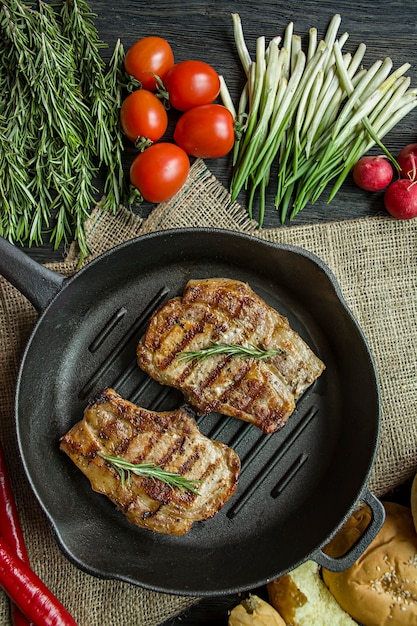 Steak grillé sur une poêle ronde, garni d&#39;épices pour la viande, le romarin, les légumes verts et les légumes sur un bois foncé