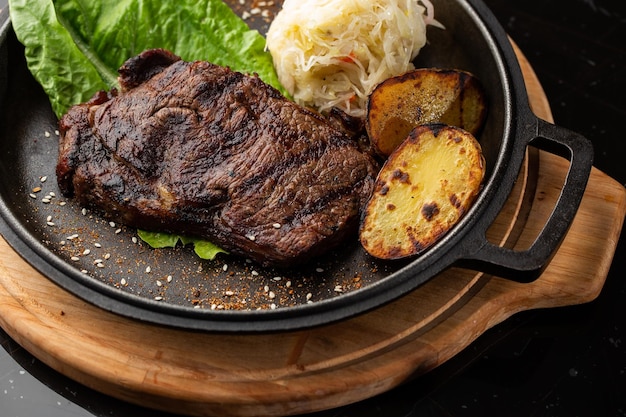 Steak grillé avec pommes de terre dorées au four servies avec du chou aigre et de la sauce rouge sur fond sombre Recette délicieuse Filet de porc cuit à la poêle pour le dîner Texture de viande juteuse frite