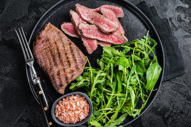 Steak de jupe grillé au barbecue sur une assiette avec salade verte Fond noir Vue de dessus