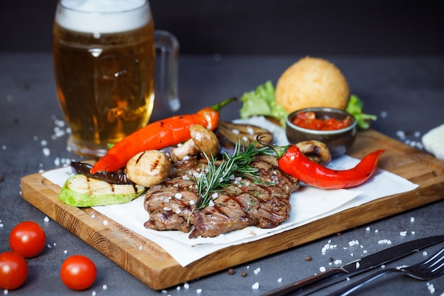 steak avec légumes cuits au four sur une assiette et une pinte de bière en arrière-plan