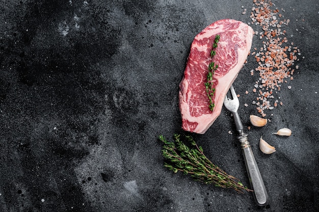 Steak de New York cru sur une table de boucher avec du sel et du thym